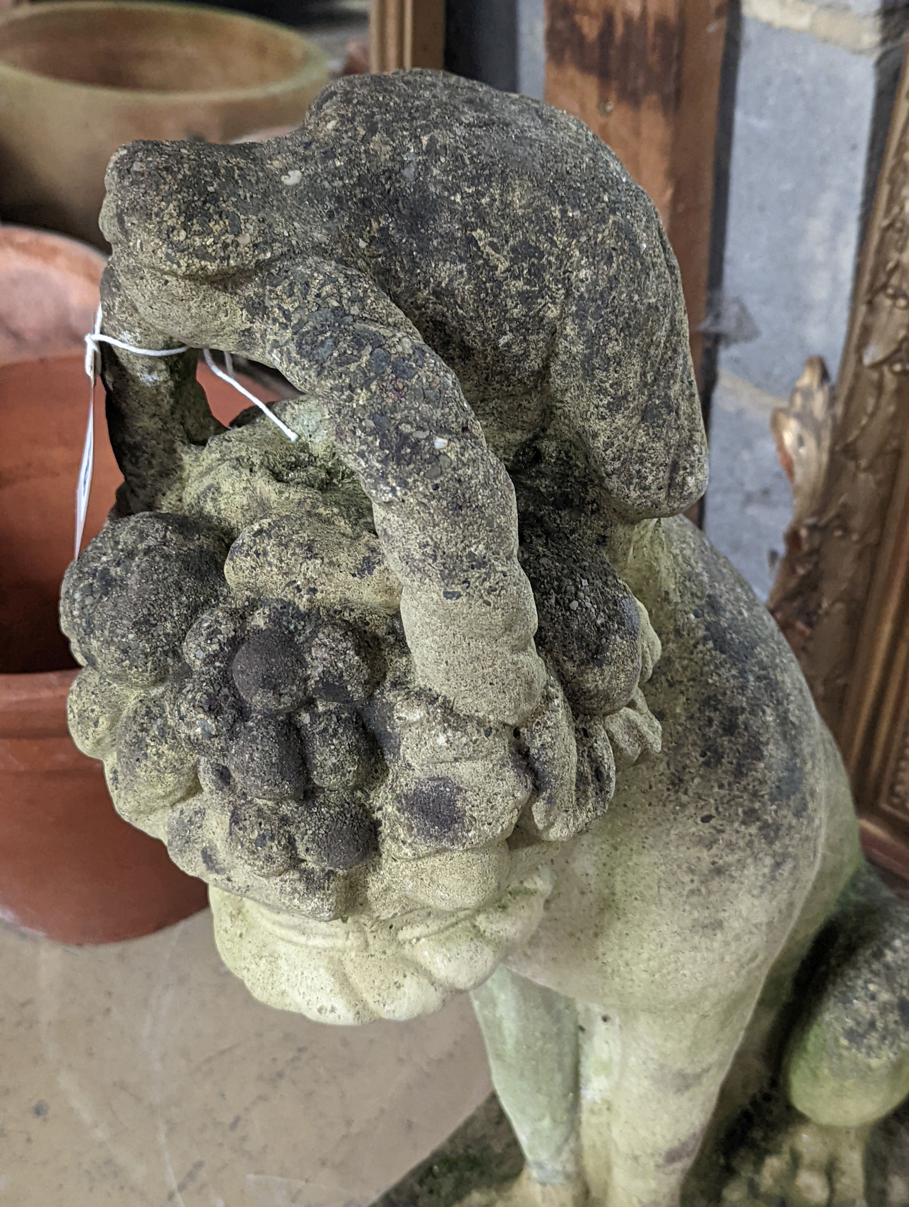 A reconstituted stone garden ornament of a seated hound, a basket of fruit in its mouth, height 60cm